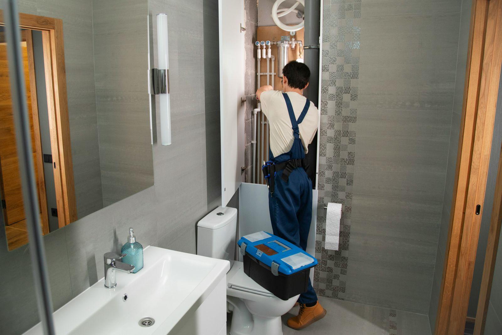Een installateur met gereedschapskist werkt aan de leidingen in een badkamer